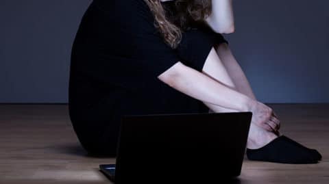 Woman in dark rook looking at her lit up laptop