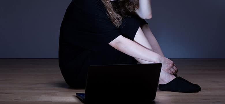 Woman in dark rook looking at her lit up laptop