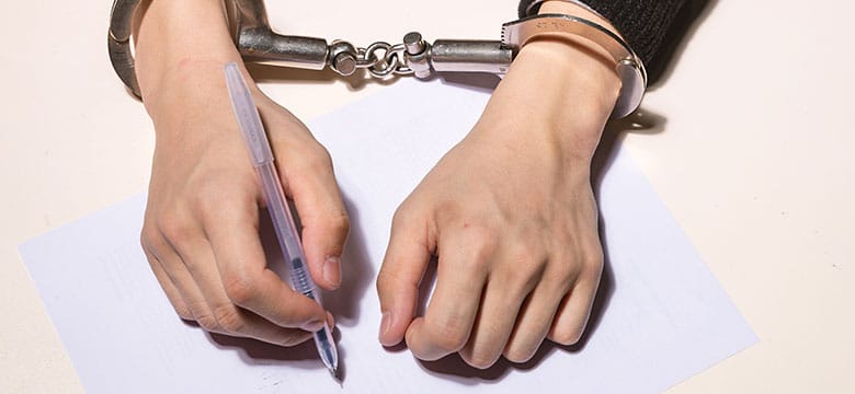 Person's hands in handcuffs writing answers on a questioning form