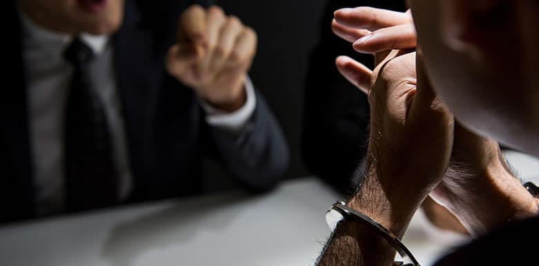 Man in handcuffs talking to police officer in a darkened room