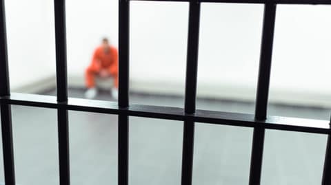 Man in jumpsuit sitting behind bar image