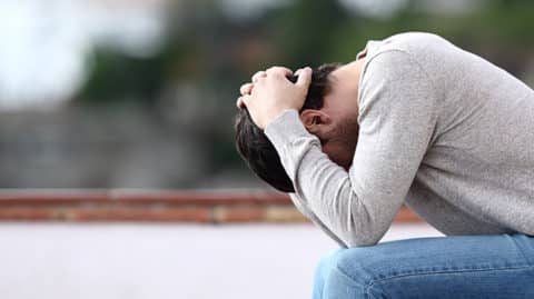 Upset man holding head on park bench