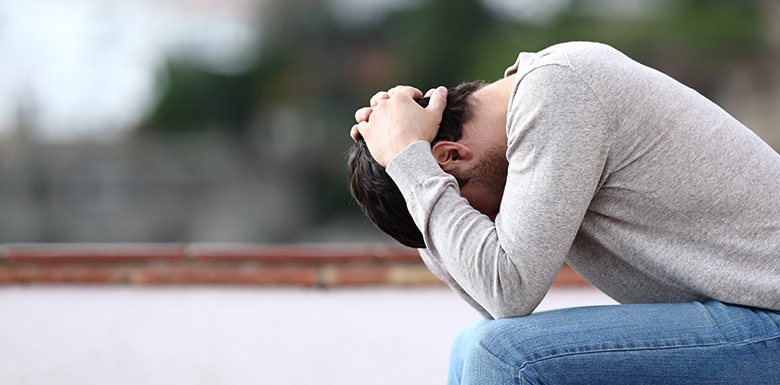 Upset man holding head on park bench