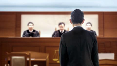 Back of man facing three judges in wood paneled court room