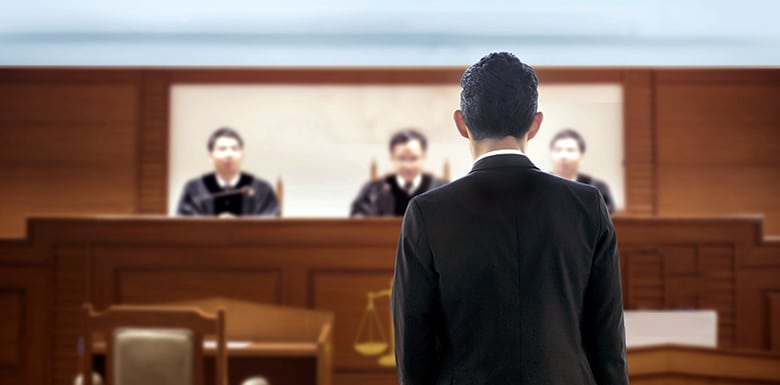 Back of man facing three judges in wood paneled court room