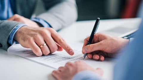 Man pointing and telling another man where to sign a document