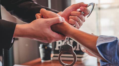 Officer reaching across desk to remove handcuffs from man