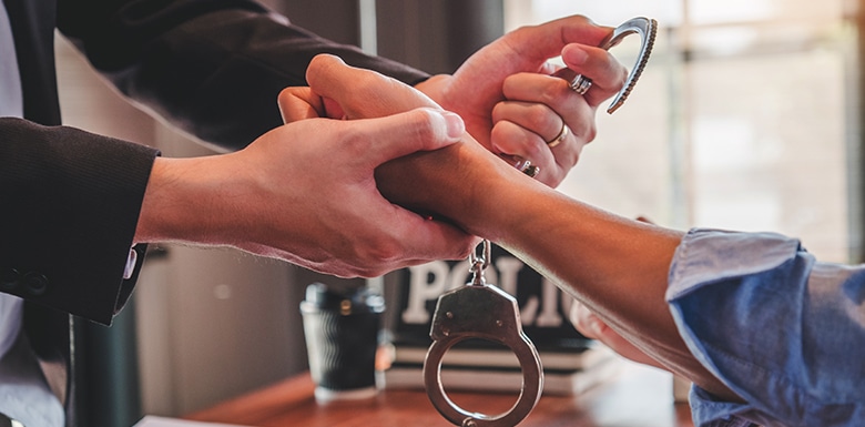 Officer reaching across desk to remove handcuffs from man