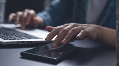 Man reaching for phone while using laptop