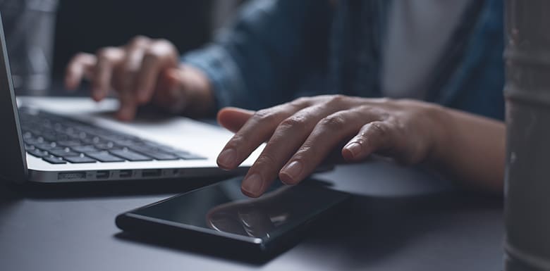 Man reaching for phone while using laptop