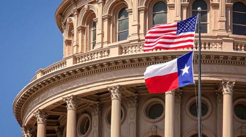 USA flag and Texas flag flying in front of old stately building