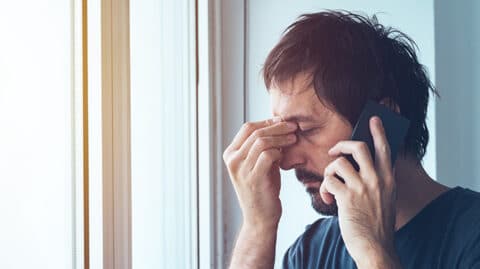 Man pinching face in worry while talking on the phone