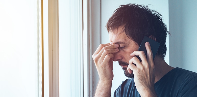 Man pinching face in worry while talking on the phone