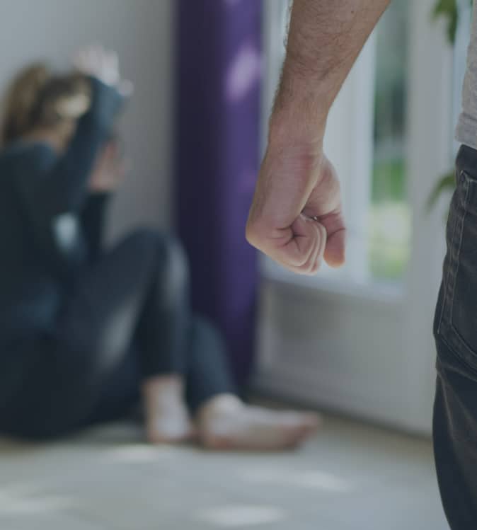 man making a fist, woman cowering in the corner of a room